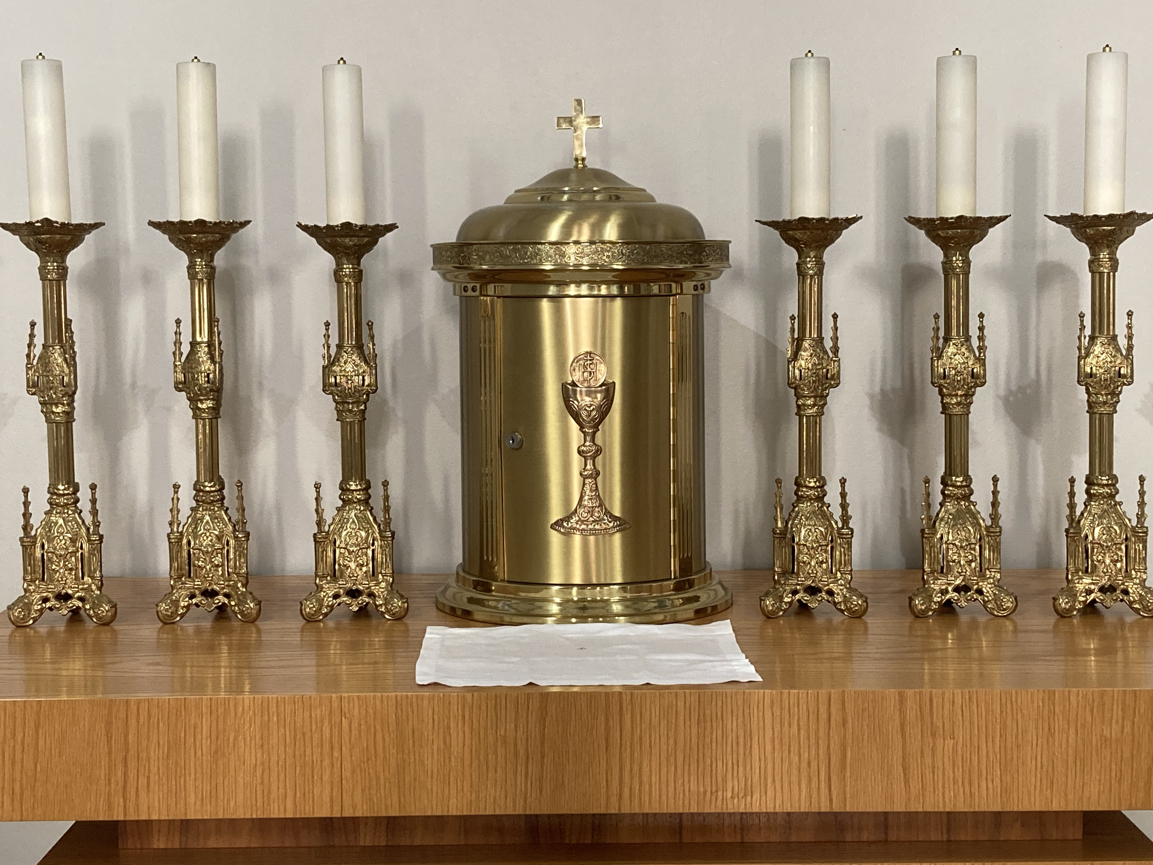 Image of gold tabernacle with three white candles on a golden stand on either side. This is all placed on a wooden table